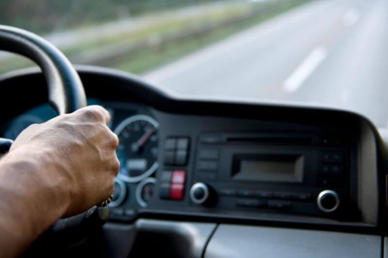 Mão segurando um volante com um painel de caminhão ao fundo