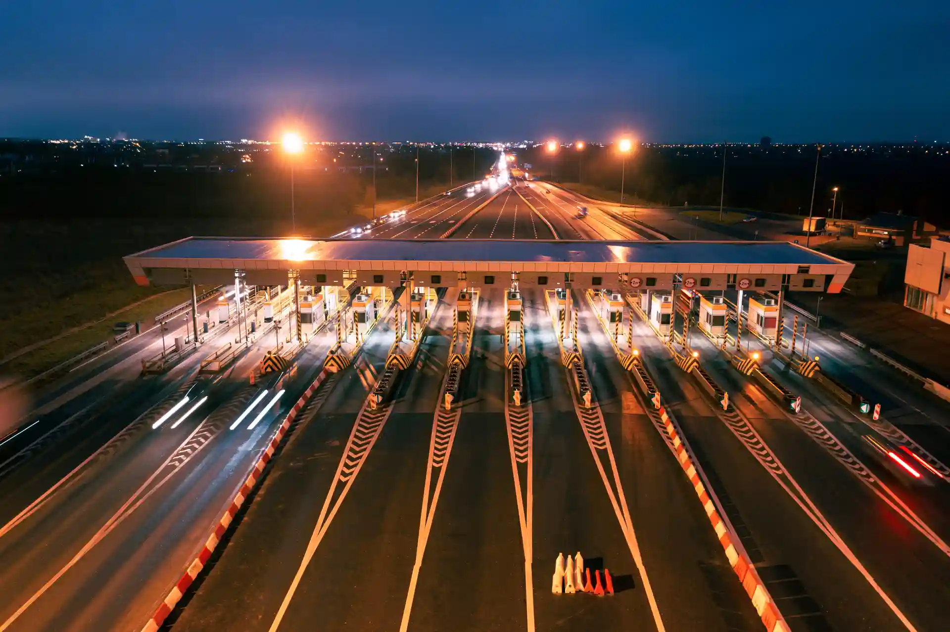 Pedágio free flow: o que é e como funciona? Vista noturna de praça de pedágio free flow iluminada com estradas e veículos passando, capturando a movimentação e a infraestrutura de transporte